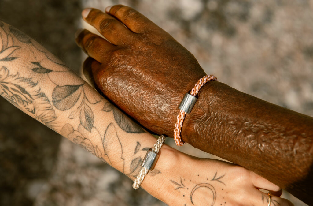 poignet de femme blanche et poignet d'homme noir portant le même bracelet dans des couleurs différentes