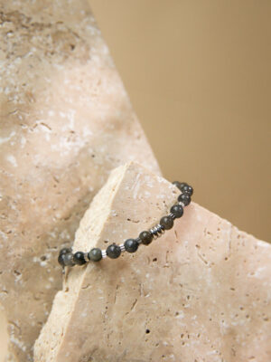 Bracelet en labradorite noire, posé sur une pierre de granite beige