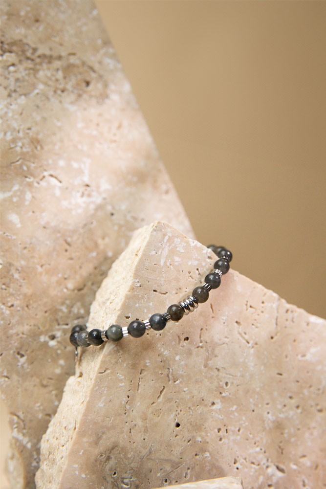 Bracelet en labradorite noire, posé sur une pierre de granite beige